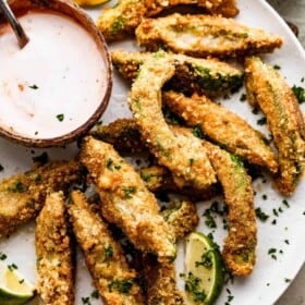overhead shot of air fried avocado fries arranged on a white plate with a small bowl of ranch dipping sauce also served on the plate.