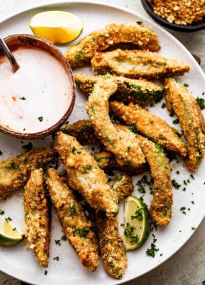 overhead shot of air fried avocado fries arranged on a white plate with a small bowl of ranch dipping sauce also served on the plate.