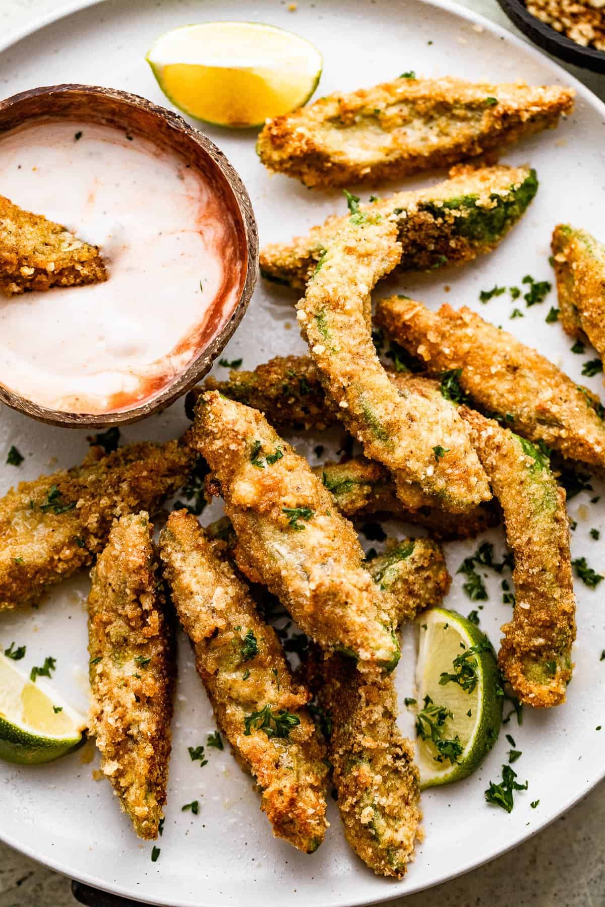 Overhead image of air fried avocado fries arranged on a white plate with a small bowl of ranch dipping sauce also served on the plate.