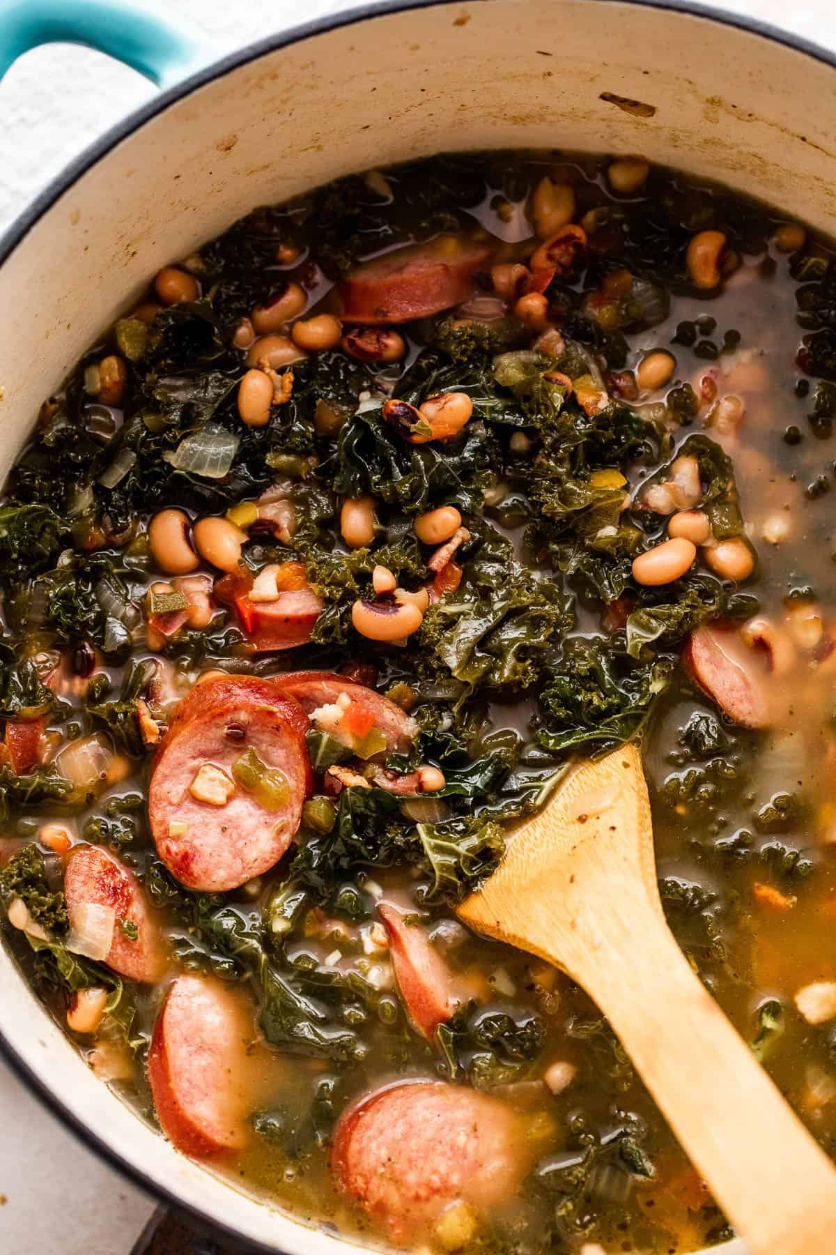 overhead shot of a wooden spoon stirring through black eyed peas soup in a Dutch oven.