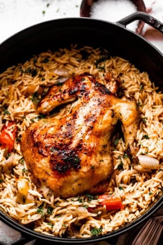 overhead shot of a dutch oven filled with orzo, vegetables, and a whole roast chicken on top.