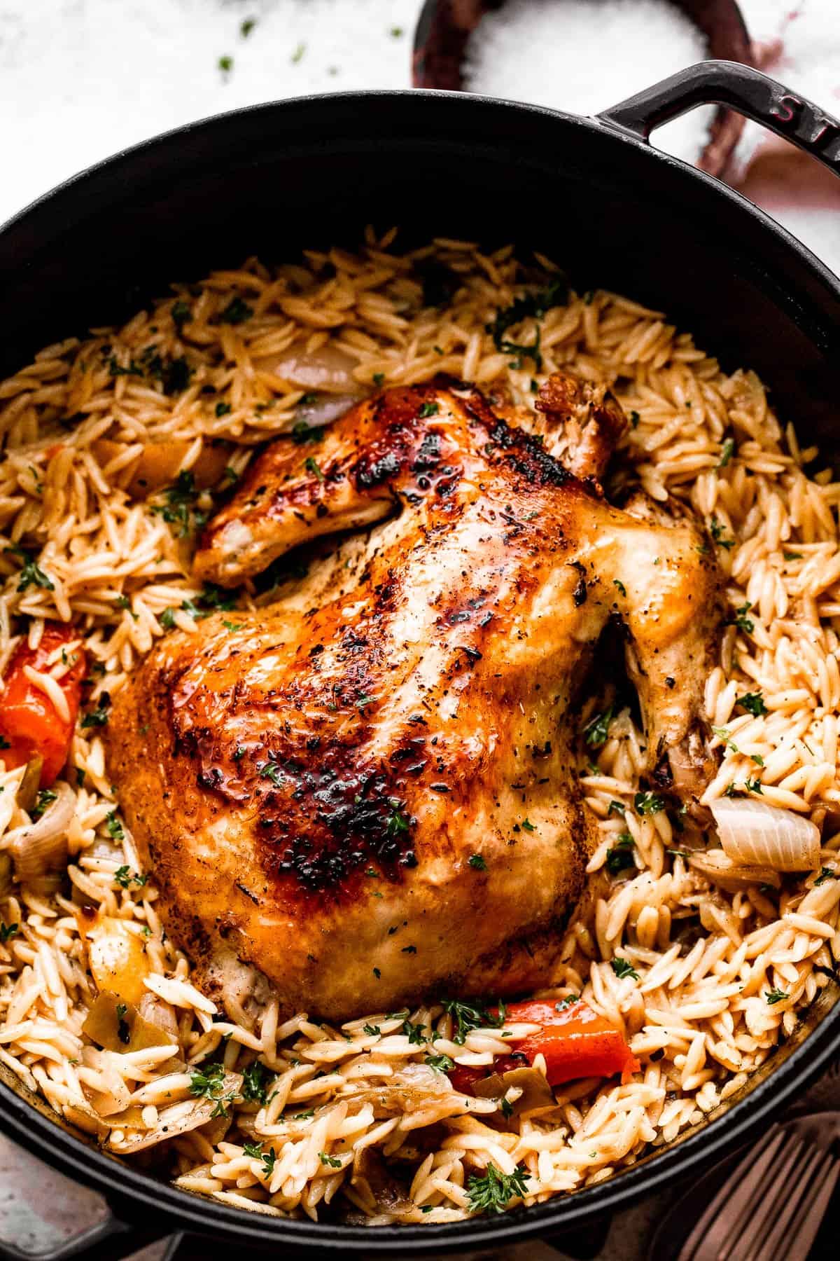 overhead shot of a dutch oven filled with orzo, vegetables, and a whole roast chicken on top.