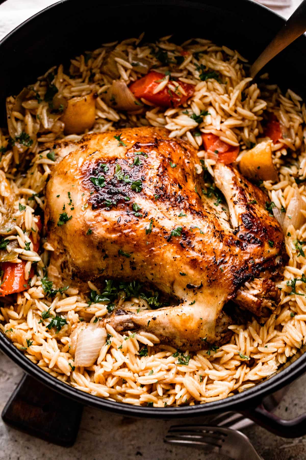 overhead shot of a whole cooked chicken set atop of cooked orzo and vegetables.