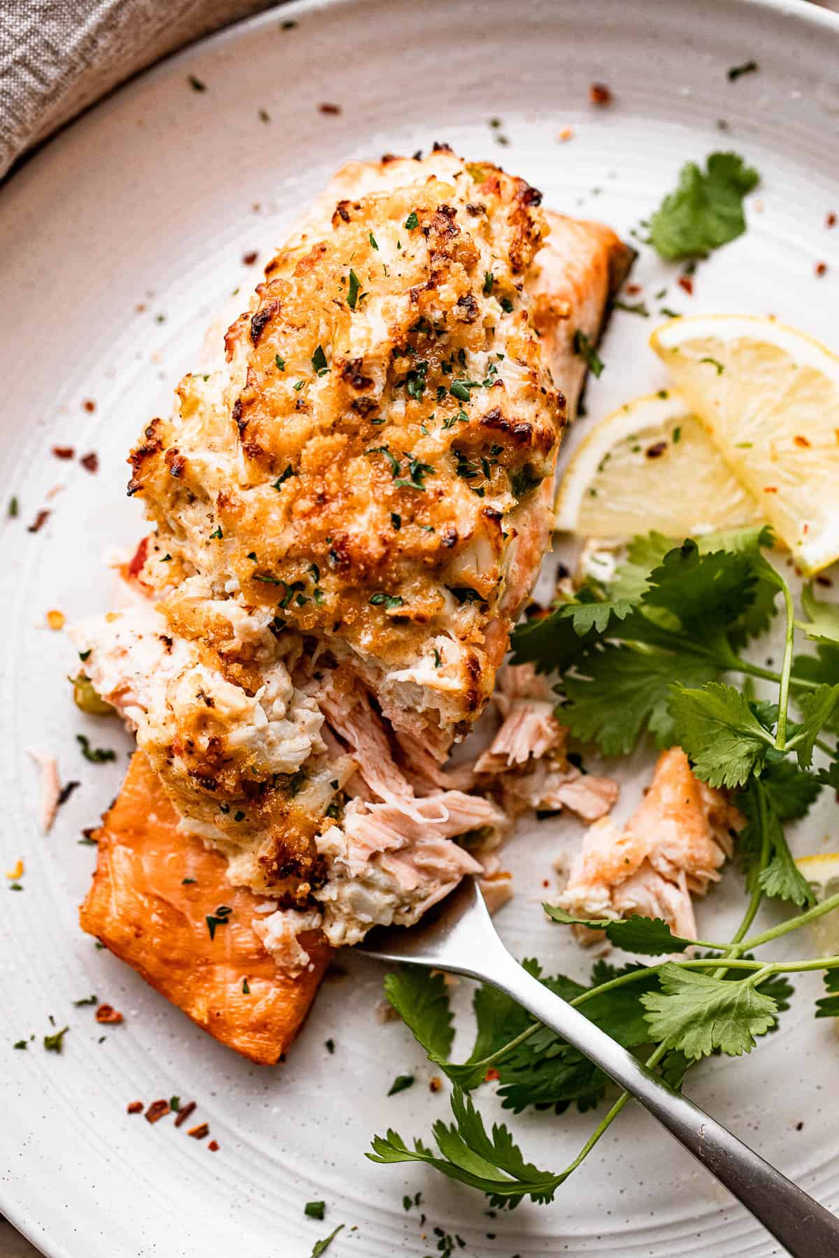 crab stuffed salmon fillet served on a white plate with greens and lemon slices arranged around it.