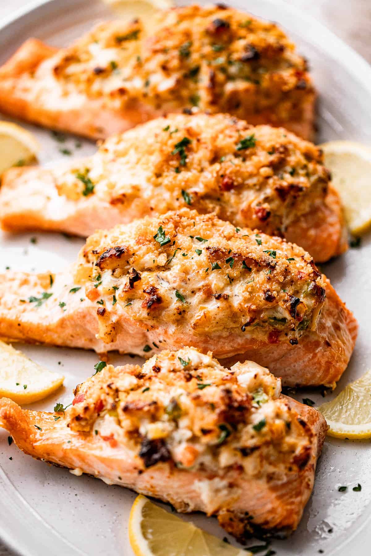 Side shot of four crab stuffed salmon fillets arranged on a long oval plate.