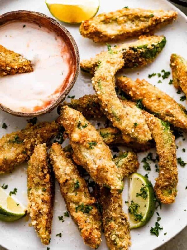 overhead shot of air fried avocado fries arranged on a white plate with a small bowl of ranch dipping sauce also served on the plate.