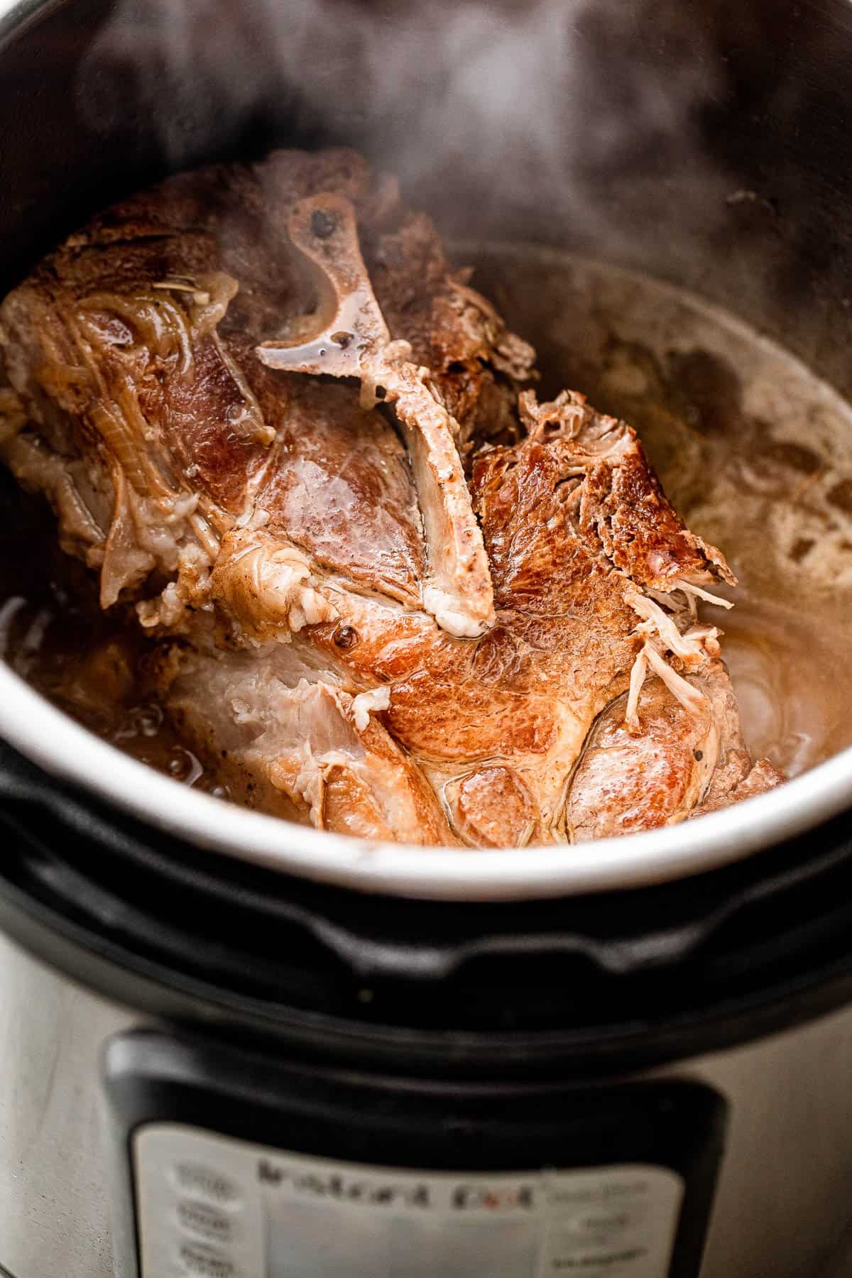 Shot of a pork shoulder inside the instant pot and steam coming out of the meat.