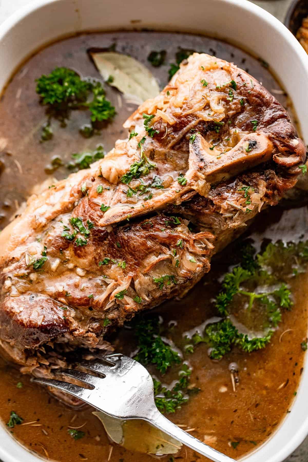 Overhead image of a cooked Pork Shoulder in a serving plate with a fork stabbed inside of it at the bottom right.