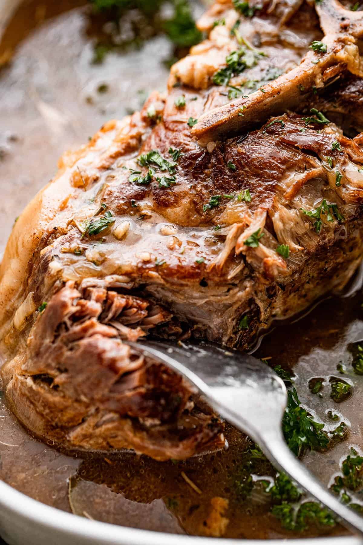 A fork tearing into a cooked pork shoulder.