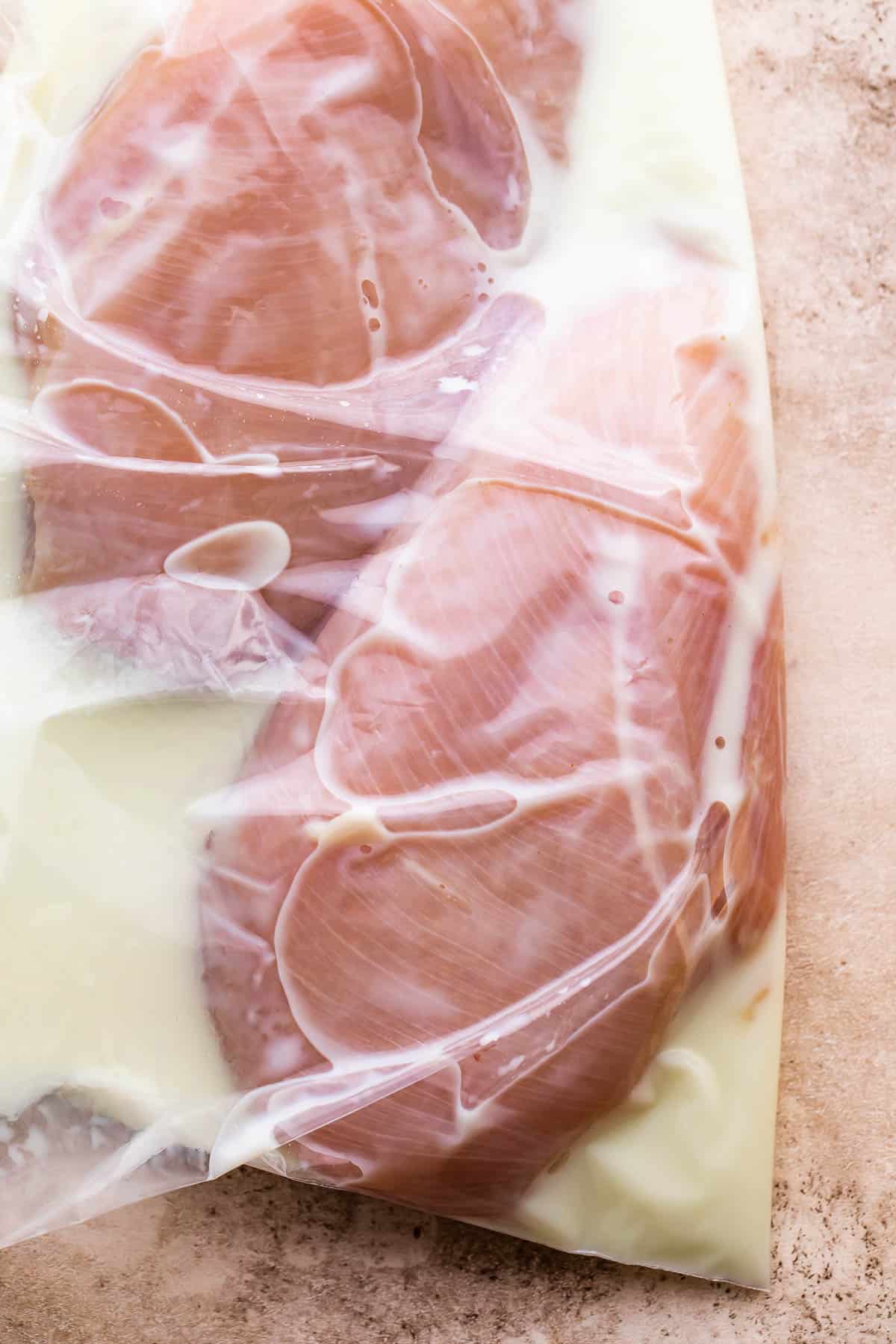 ziploc bag with two raw chicken breasts marinating in milk.