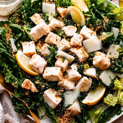 overhead shot of Lemon Kale Caesar Salad served on a plate and topped with lemons, parmesan cheese, and a sprinkle of bread crumbs.
