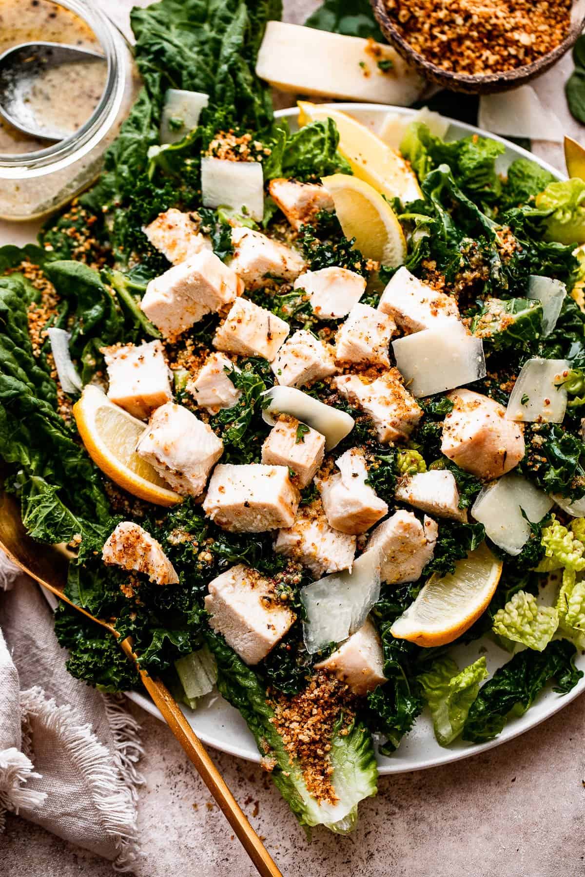 overhead shot of Lemon Kale Caesar Salad served on a plate and topped with lemons, parmesan cheese, and a sprinkle of bread crumbs.