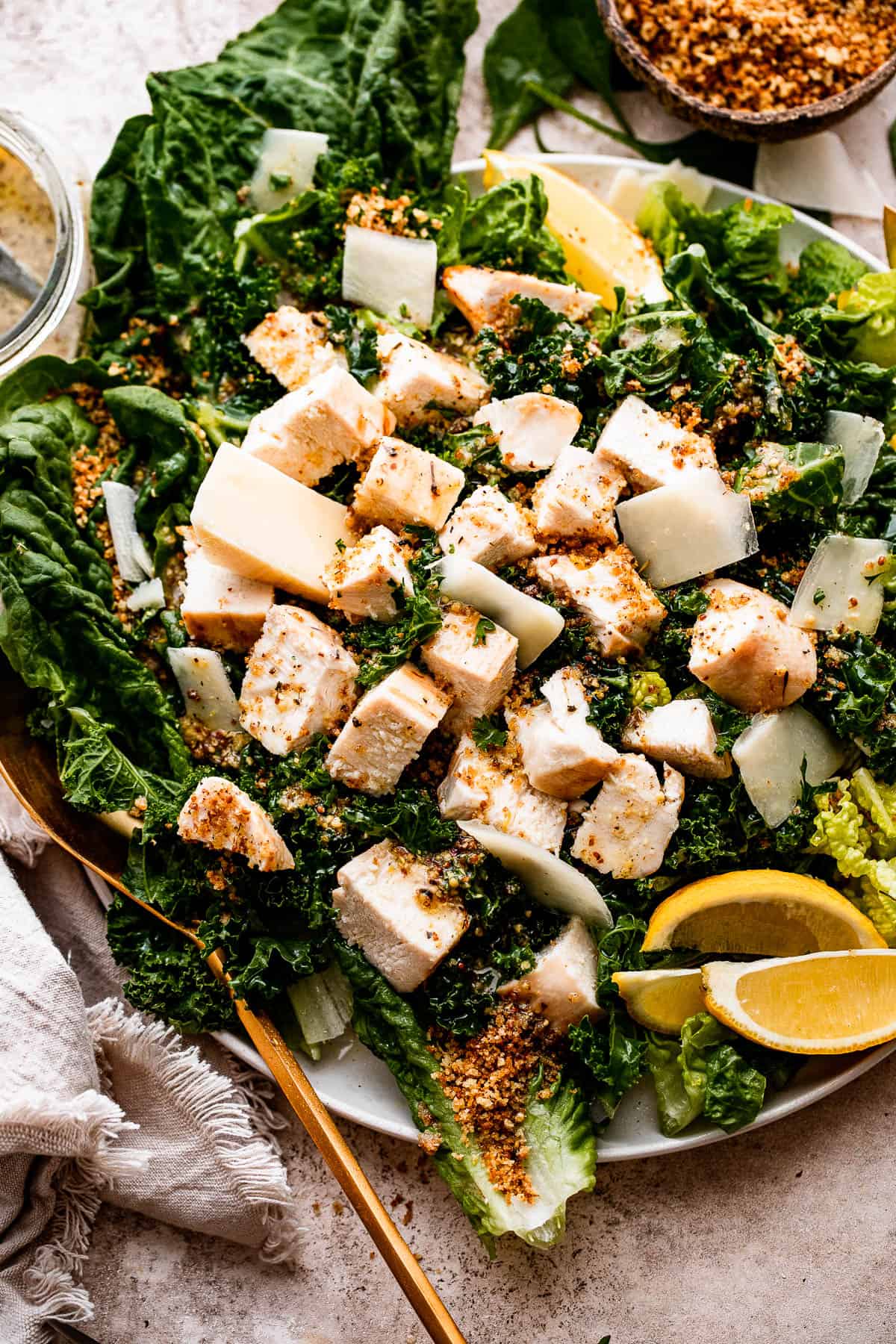 overhead shot of Lemon Kale Caesar Salad served on a plate and topped with lemons, parmesan cheese, and a sprinkle of bread crumbs.
