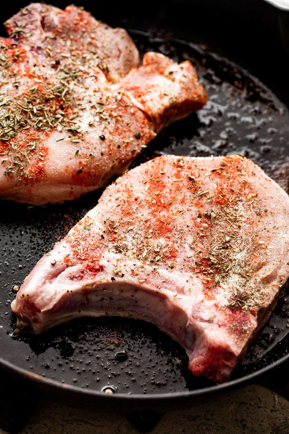 two raw pork chops cooking in a cast iron skillet