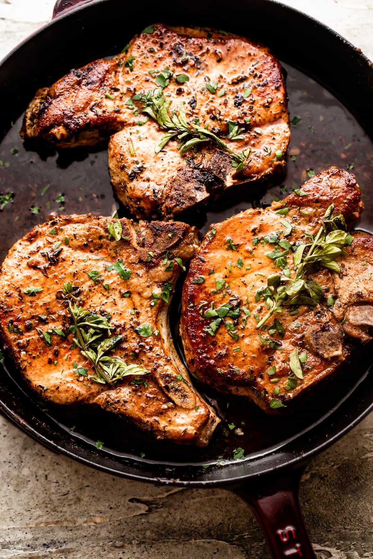 overhead shot of three oven baked pork chops arranged on a cast iron skillet and garnished with fresh herbs