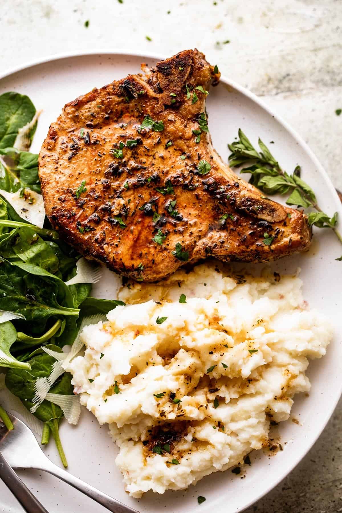 spinach salad, mashed potatoes, and a baked pork chops arranged on a white dinner plate