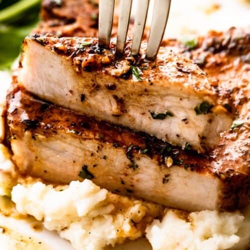 fork stabbing through a halved pork chop set on a bed of mashed potatoes