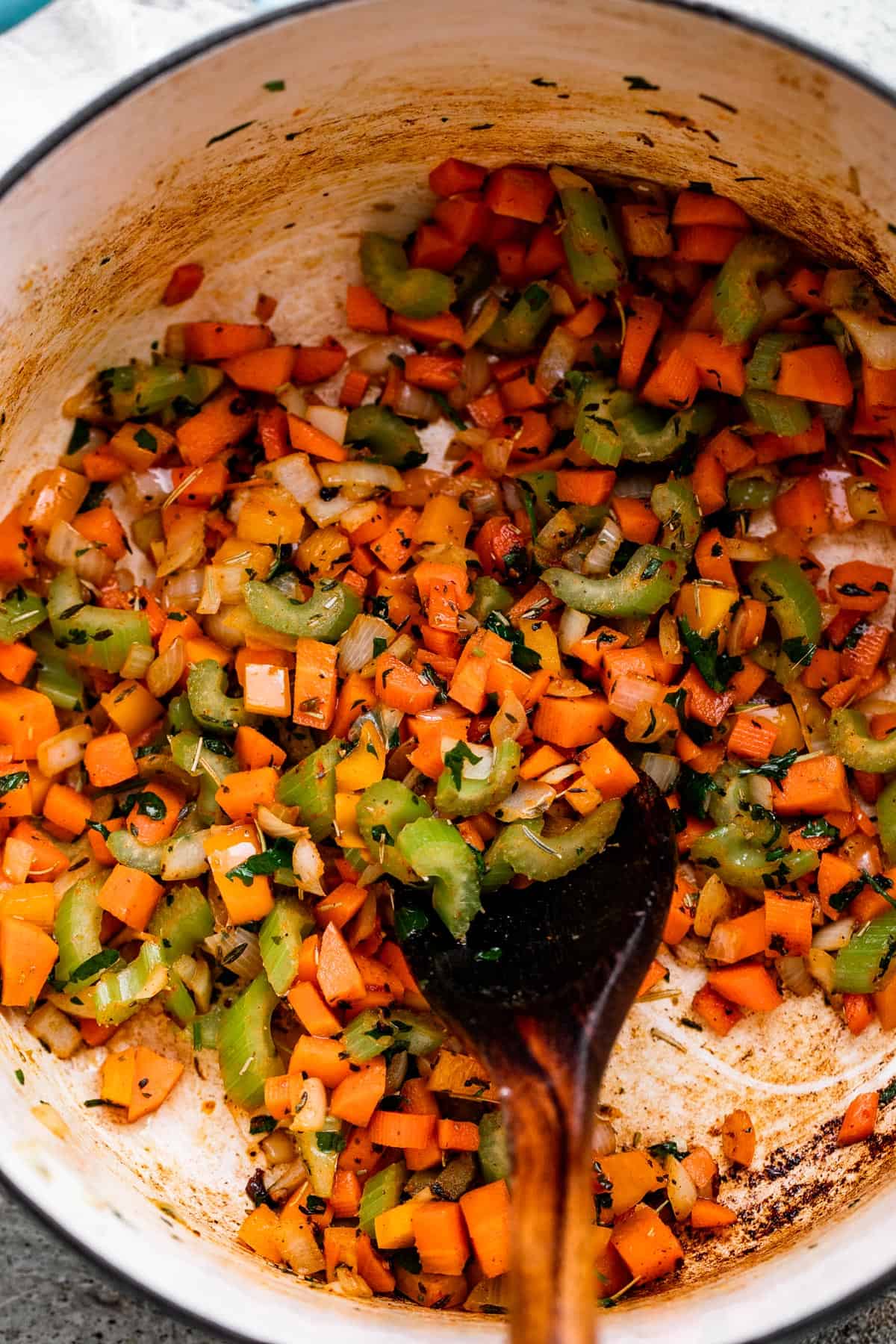 sauteeing diced carrots, onions, and celery in a Dutch Oven, with a wooden spoon stirring through it.