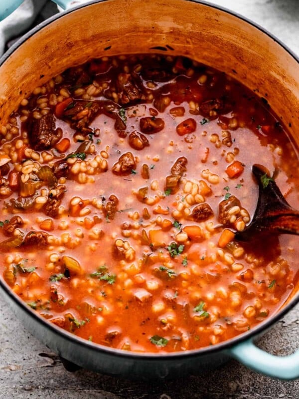 overhead shot of Beef Barley Soup in a Dutch oven and a wooden spoon placed inside the soup.