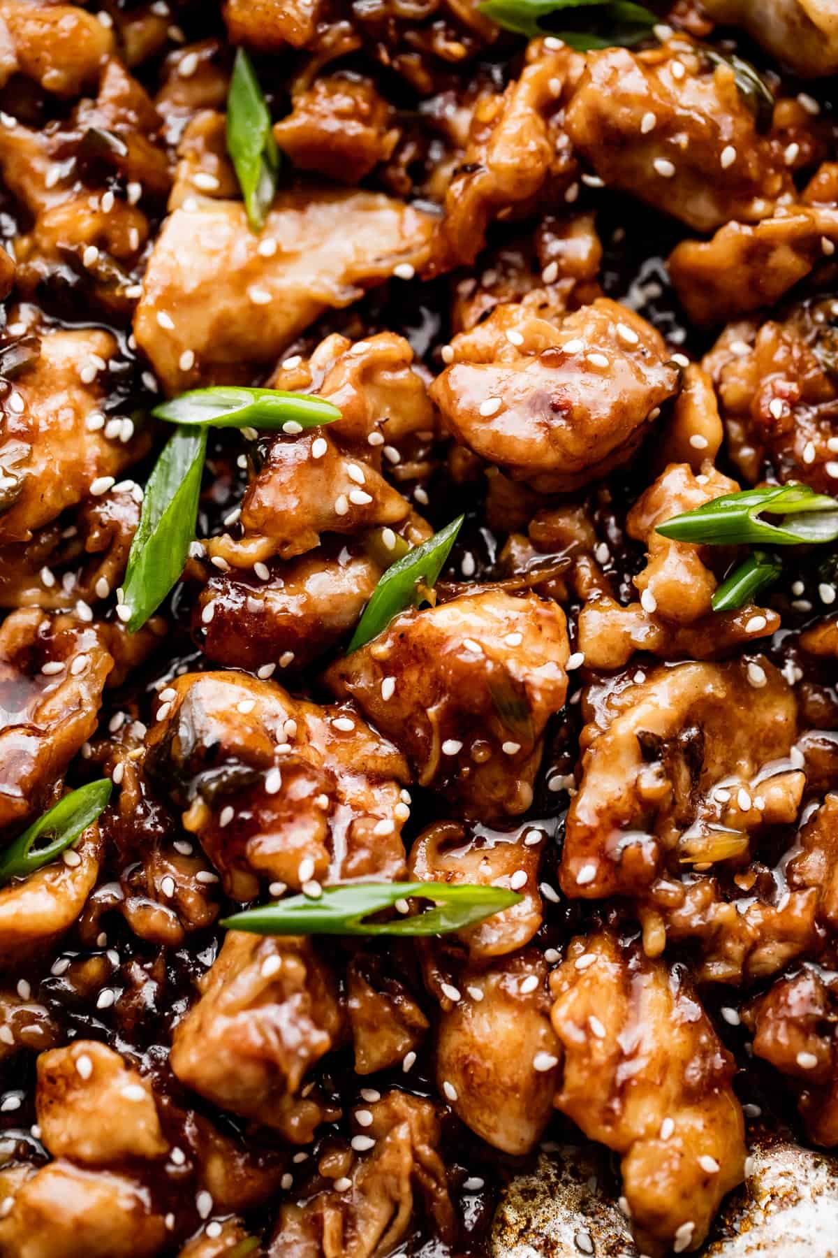 up close shot of cut up chicken thighs covered in bourbon sauce and topped with sesame seeds and sliced green onions.