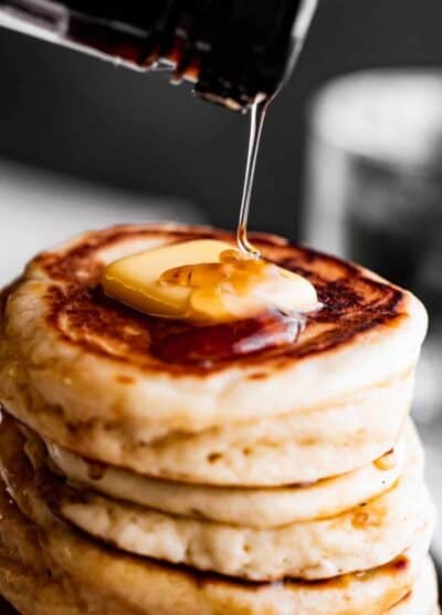 pouring pancake syrup over a stack of drop scones topped with a pat of butter.