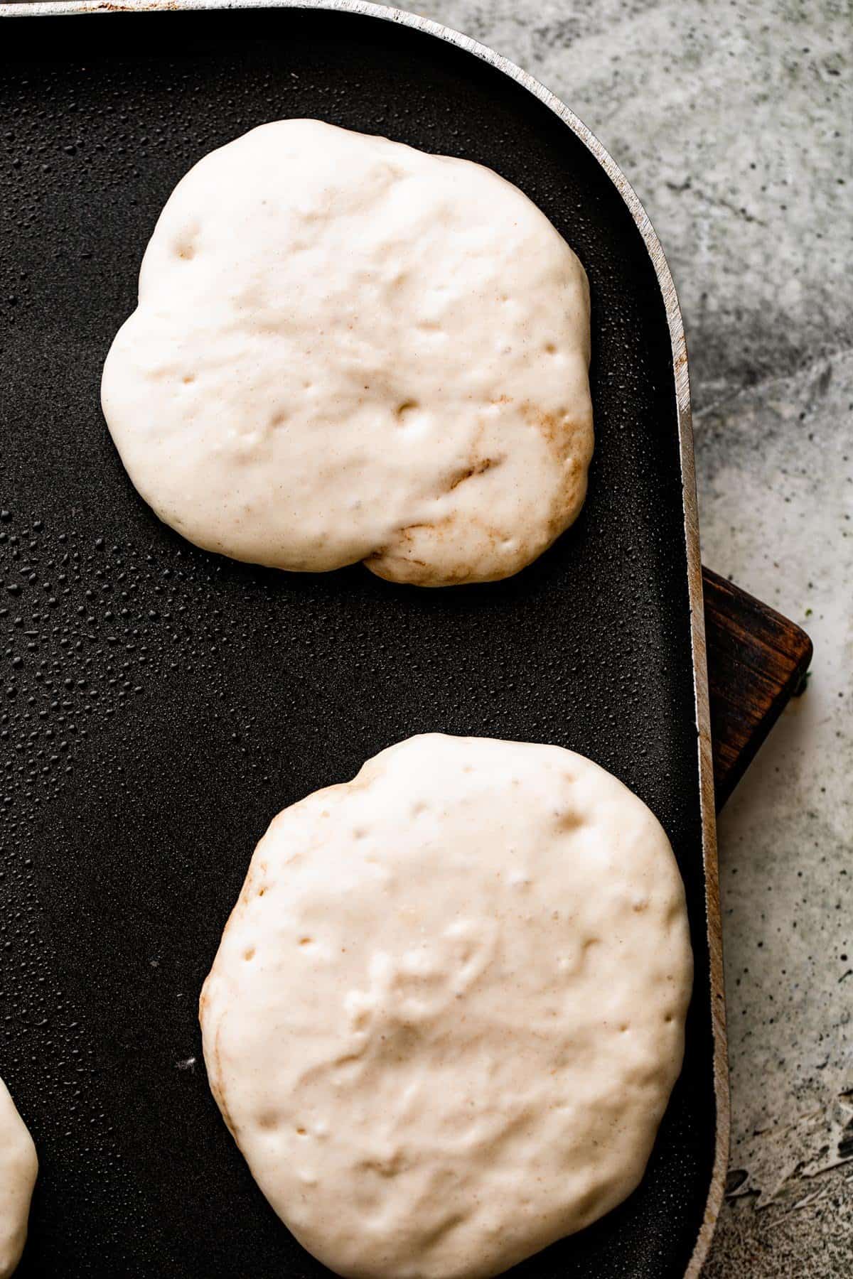 cooking two drop scones on a black pancake pan.