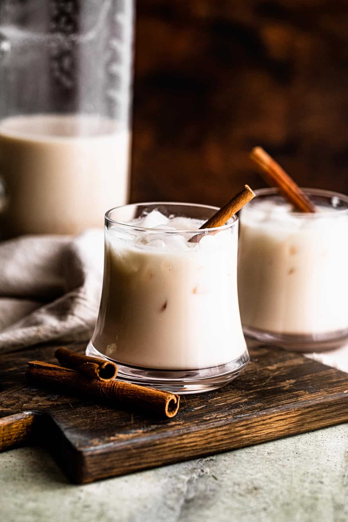 drinking glasses filled with ice cubes and horchata, and garnished with a cinnamon stick