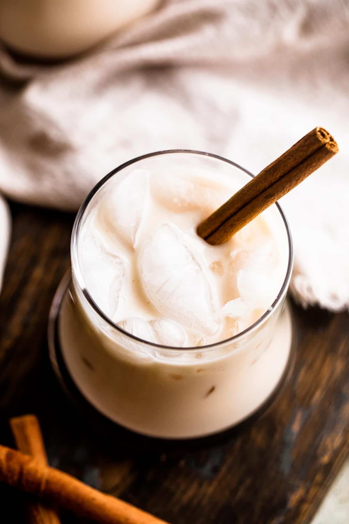 overhead shot of a drinking glass filled with ice cubes and horchata, and garnished with a cinnamon stick
