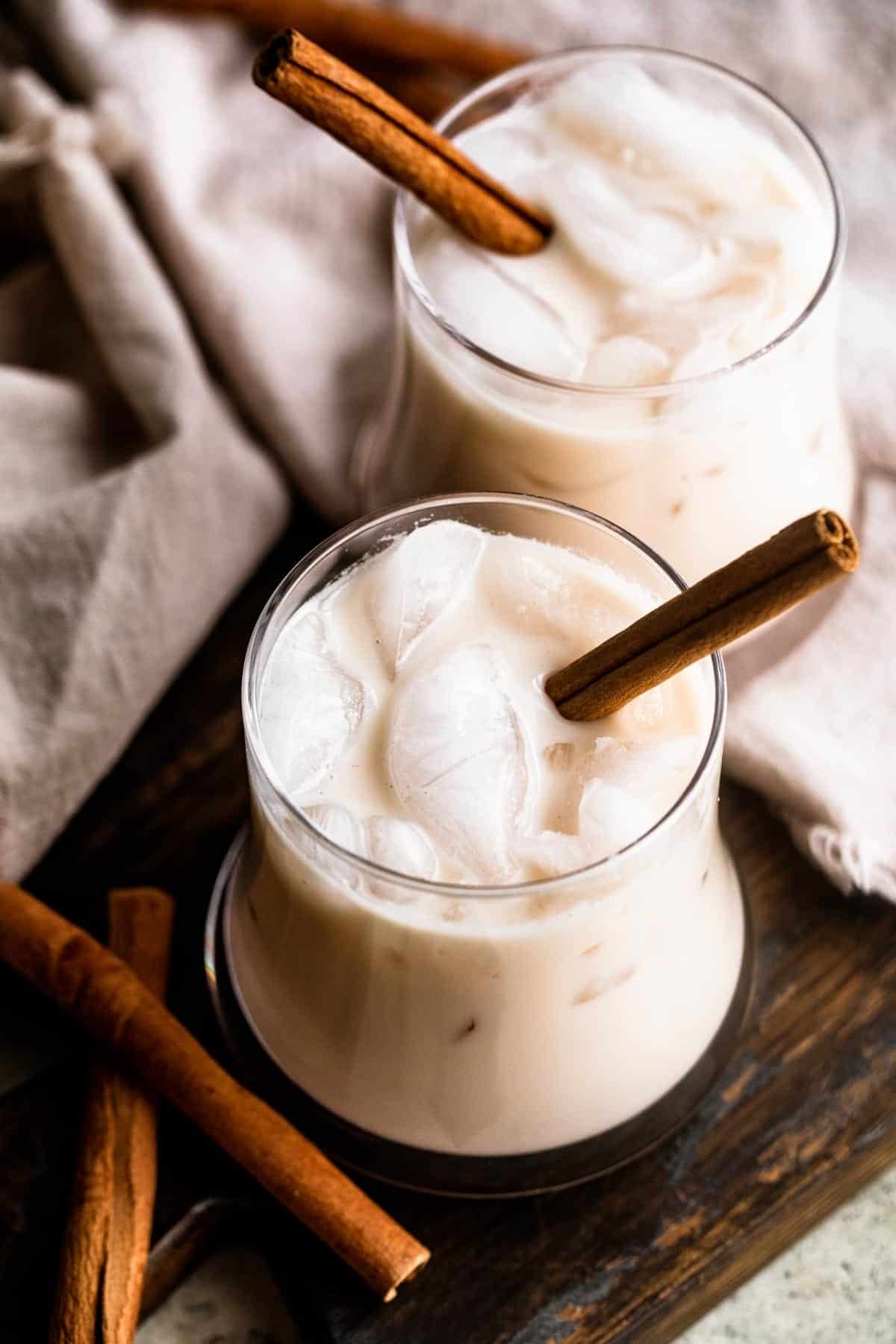 overhead shot of two drinking glasses filled with ice cubes and horchata, and garnished with a cinnamon stick