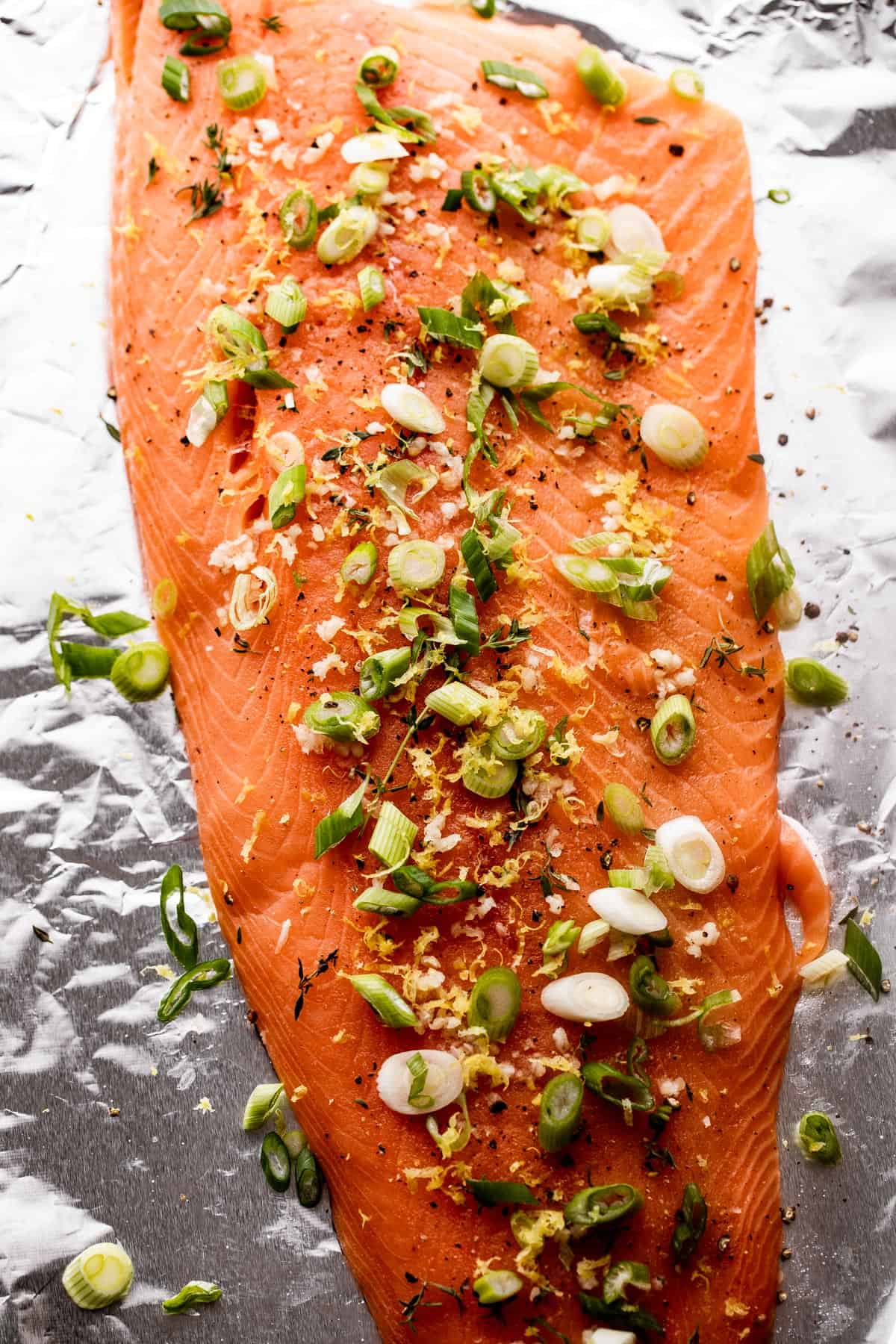 overhead shot of a raw and whole Salmon filet set on a piece of foil topped with green onions