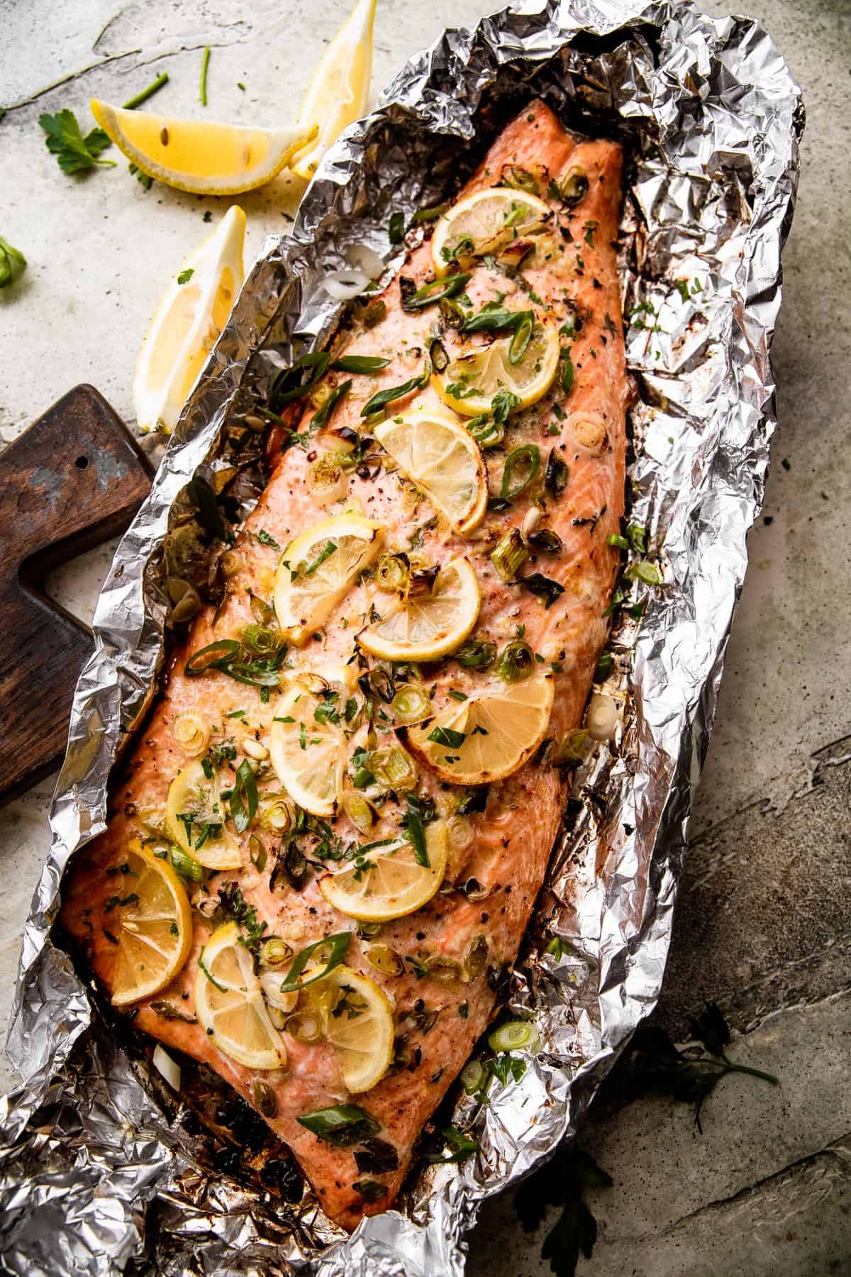 overhead shot of Lemon Butter Grilled Salmon in foil topped with green onions, sliced lemons, and parsley.