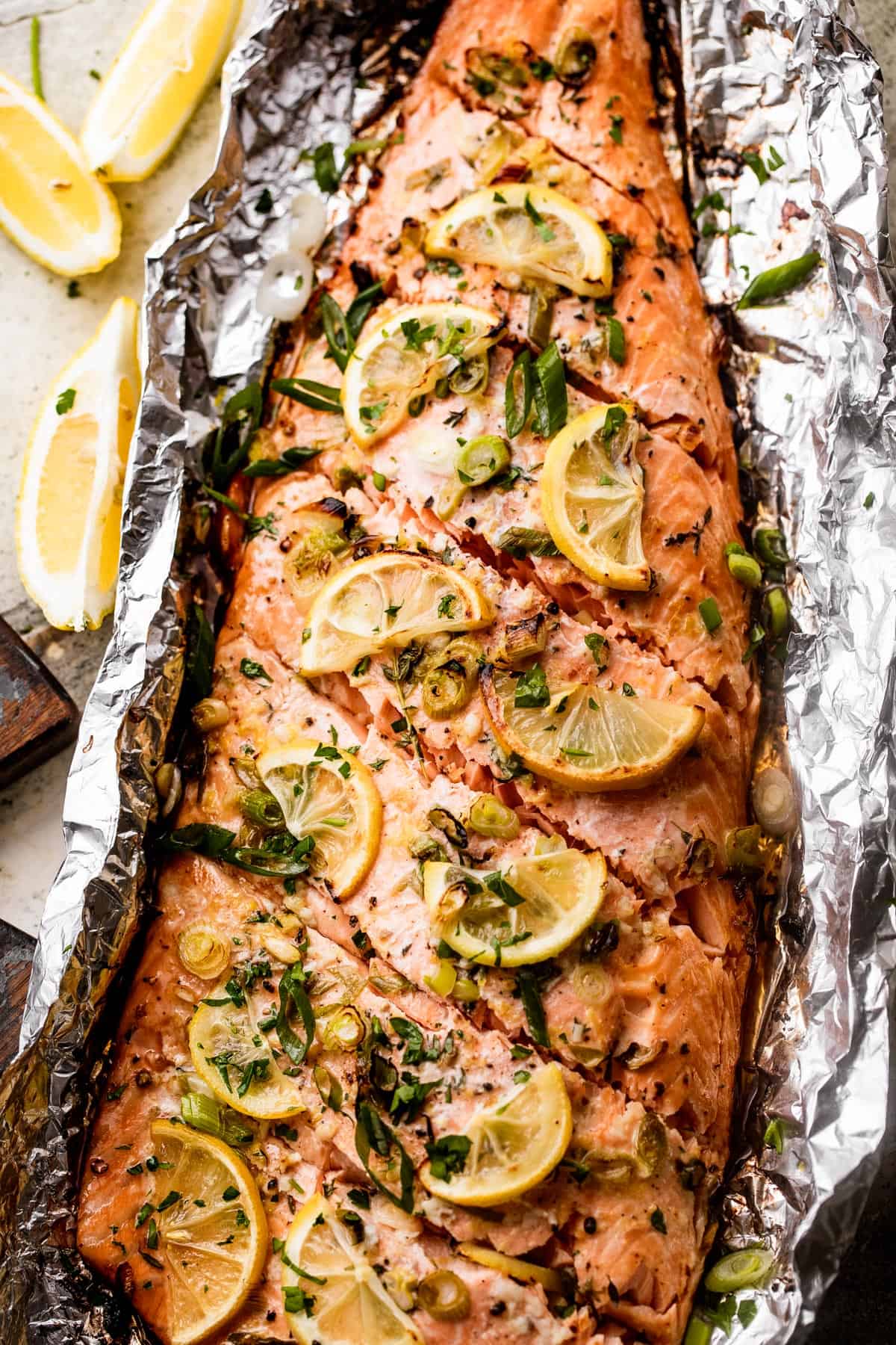 overhead shot of Lemon Butter Grilled Salmon in foil topped with green onions, sliced lemons, and parsley.