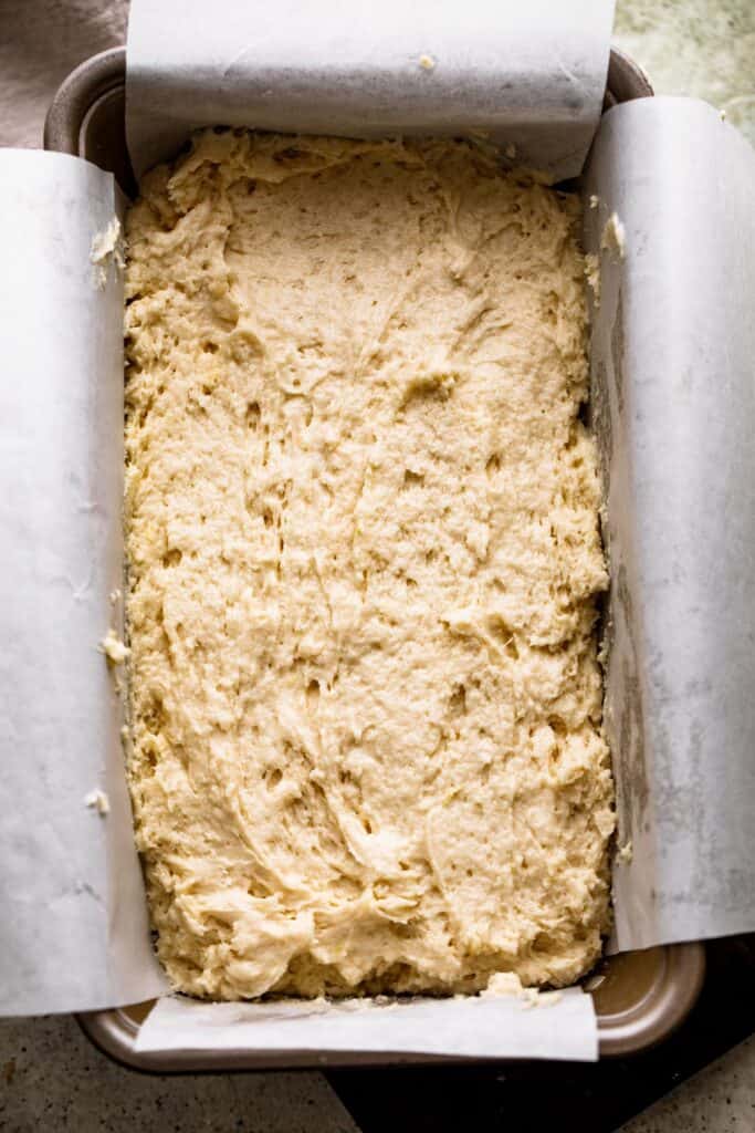 raw cake batter poured inside a loaf pan lined with parchment paper