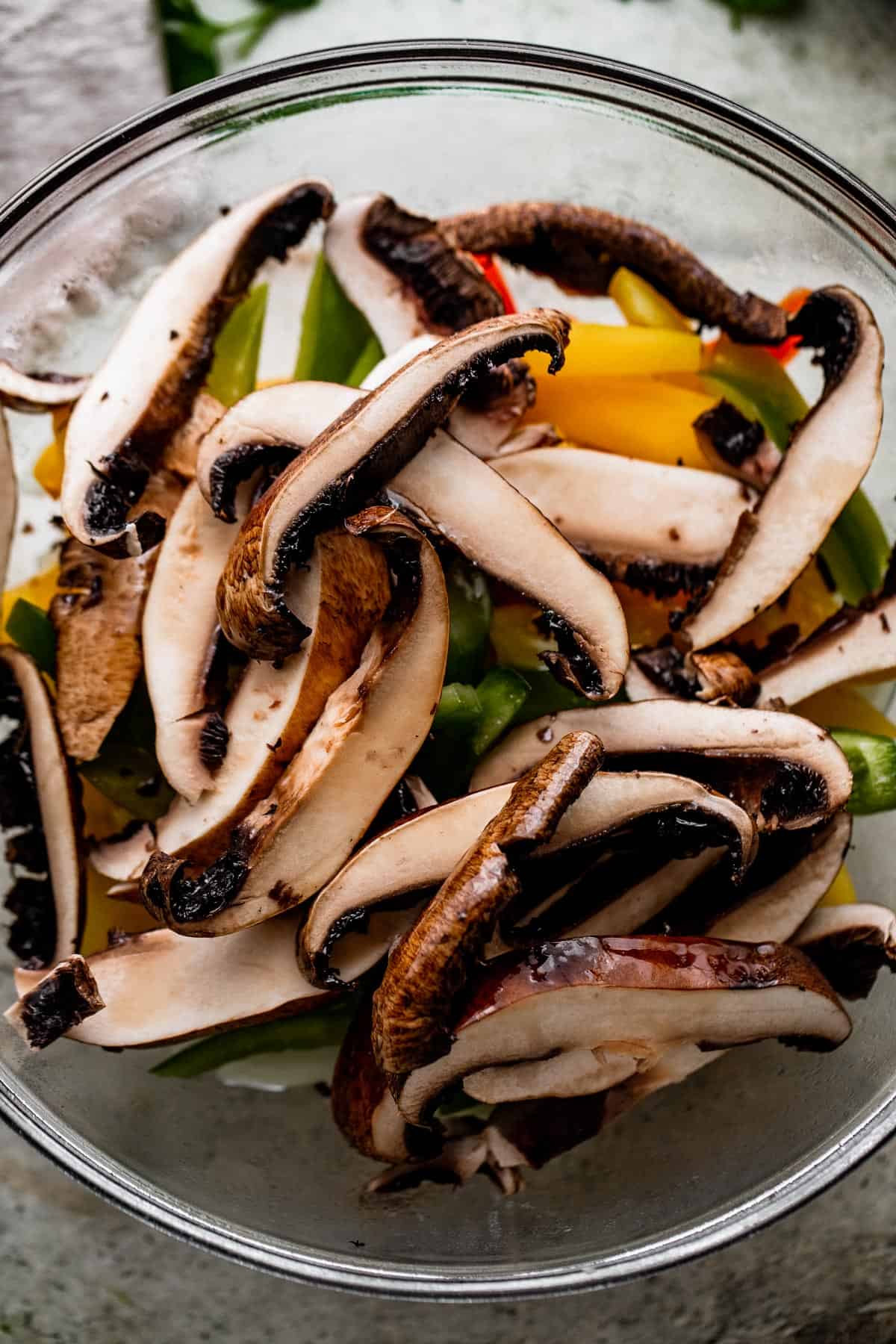 sliced portobello mushrooms, sliced bell peppers, and sliced onions inside a glass bowl