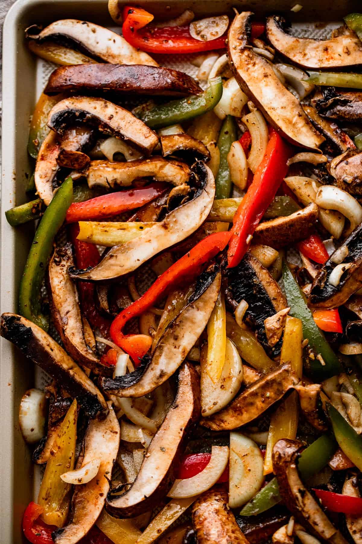 up close shot of portobello slices, pepper slices, and onion slices arranged on a gold colored baking sheet.