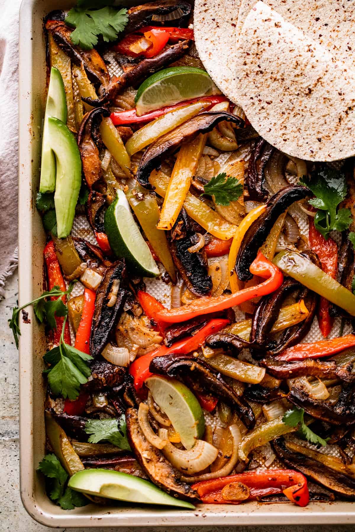 overhead shot of a baking sheet with Portobello Mushroom Fajitas and flour tortillas arranged in the top right.