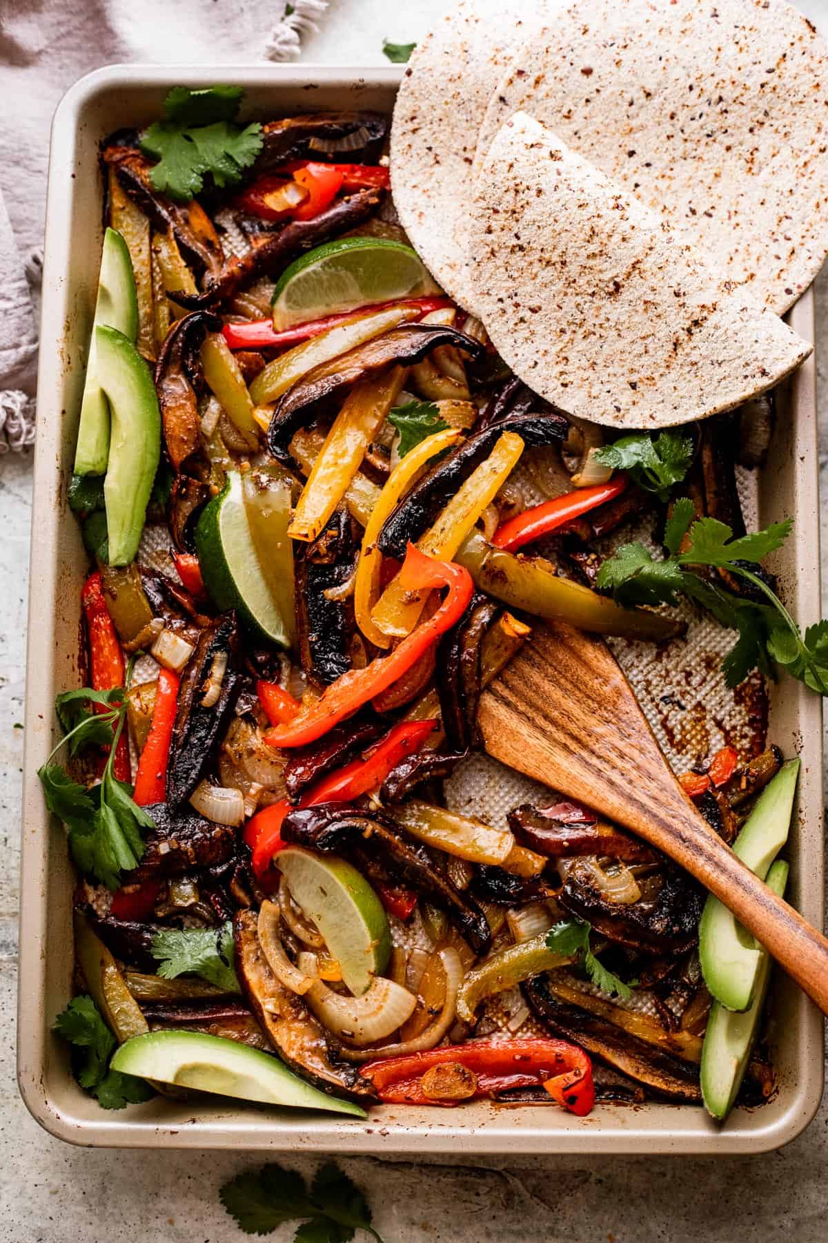 wooden spoon stirring through Portobello Mushroom Fajitas in a baking sheet