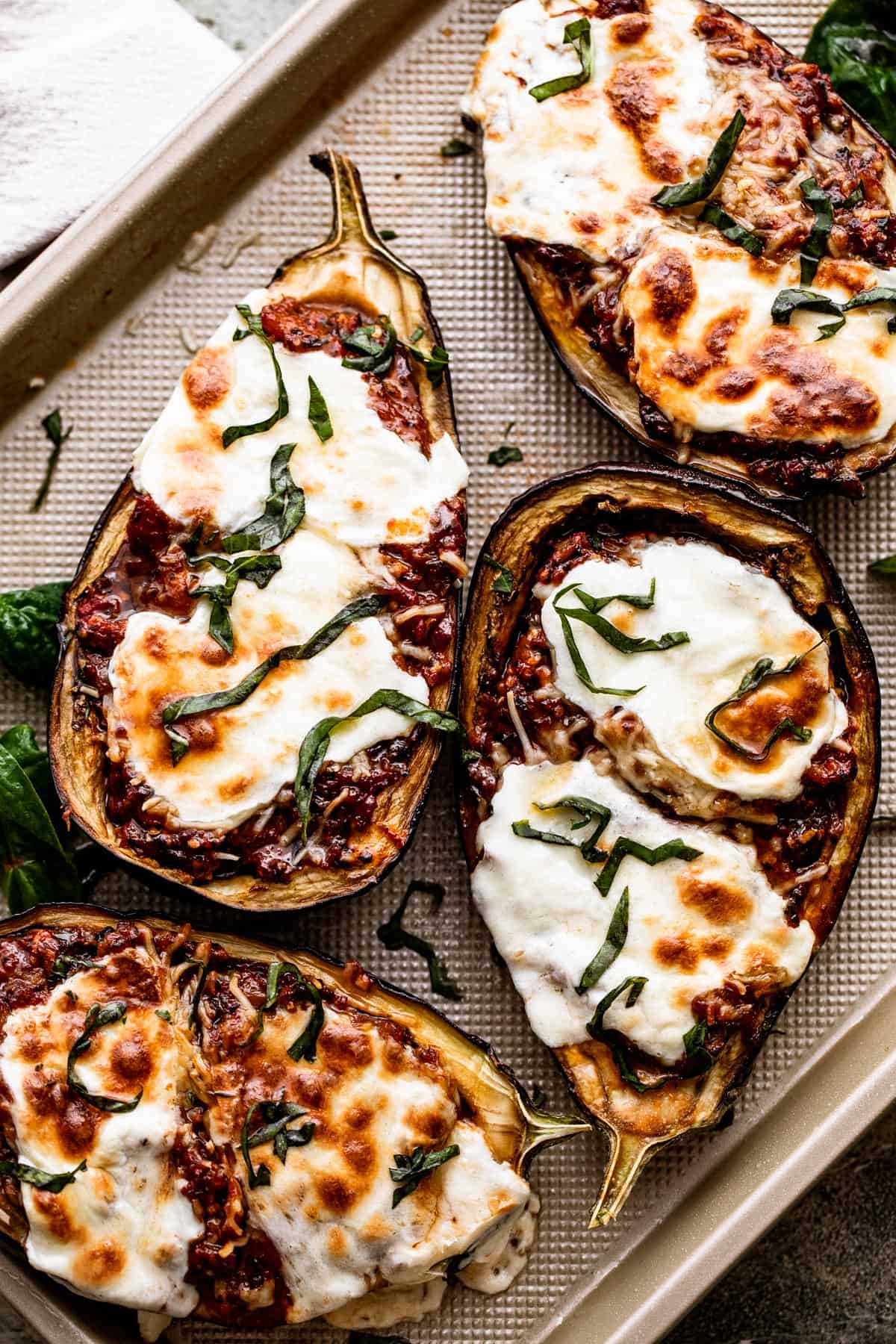 overhead shot of four Tomato Parmesan Stuffed Eggplants arranged on a gold colored baking sheet.