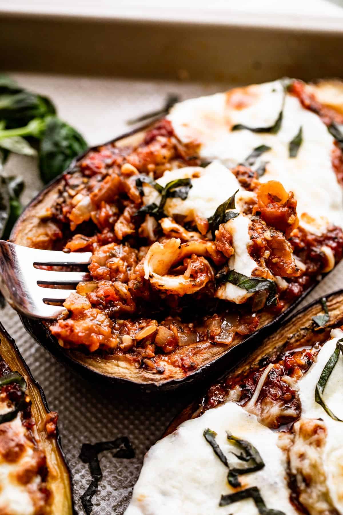 side shot of a halved eggplant stuffed with a tomato base and a fork mixing through the filling.