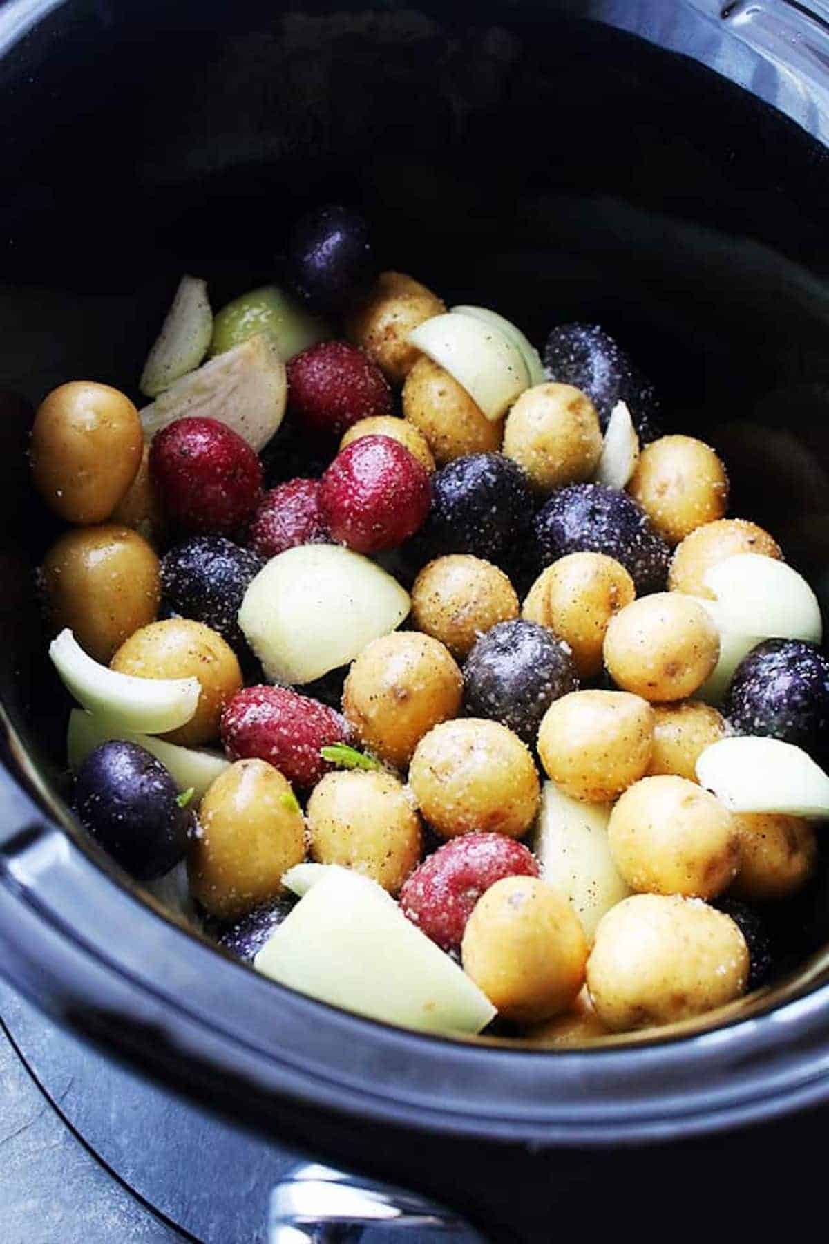 Seasoned baby potatoes and onions inside of a slow cooker