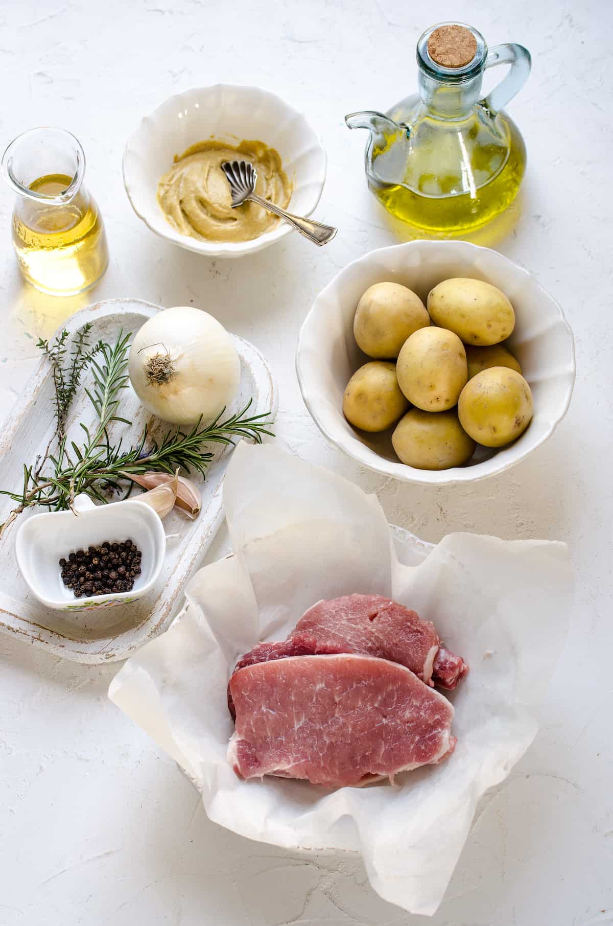 Baby potatoes, raw pork chops, olive oil and the rest of the ingredients on a kitchen countertop