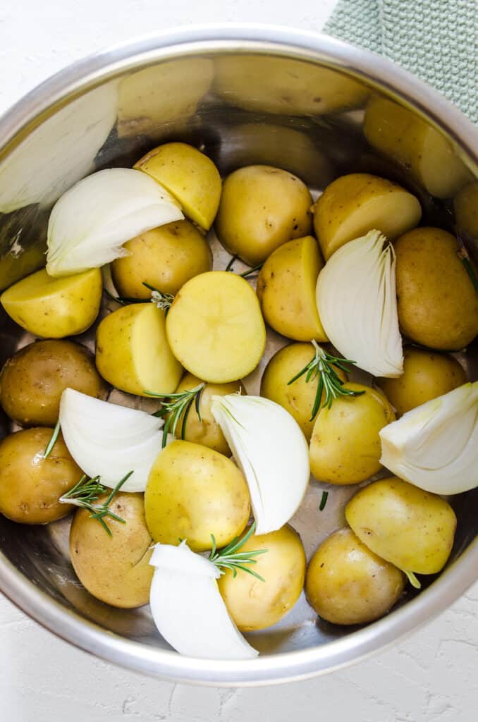 Halved baby potatoes inside of a large pot with quartered onions and some fresh rosemary