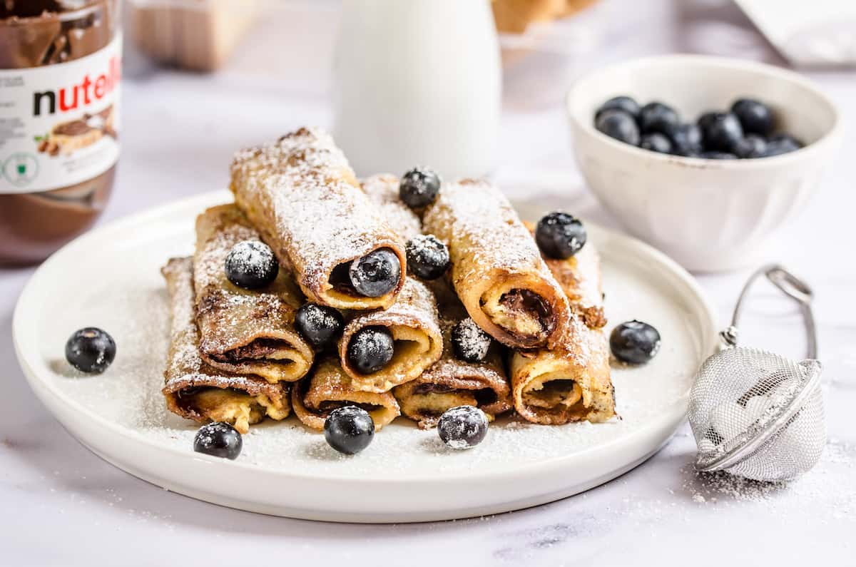 Nutella French toast roll-ups topped with powdered sugar on a plate with a raised rim