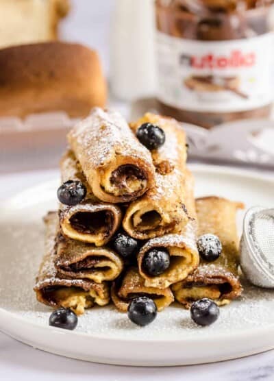 A stack of eight French toast roll-ups on a plate on top of a marble counter