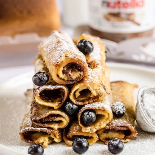A stack of eight French toast roll-ups on a plate on top of a marble counter