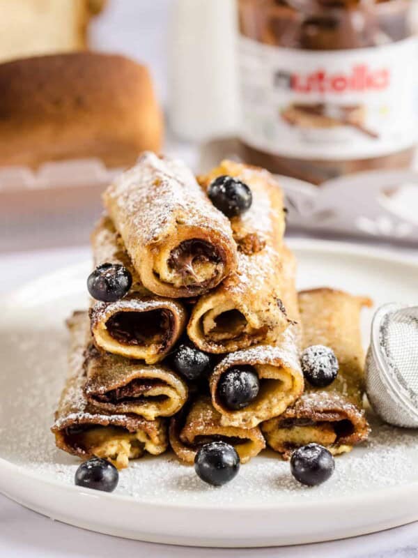 A stack of eight French toast roll-ups on a plate on top of a marble counter