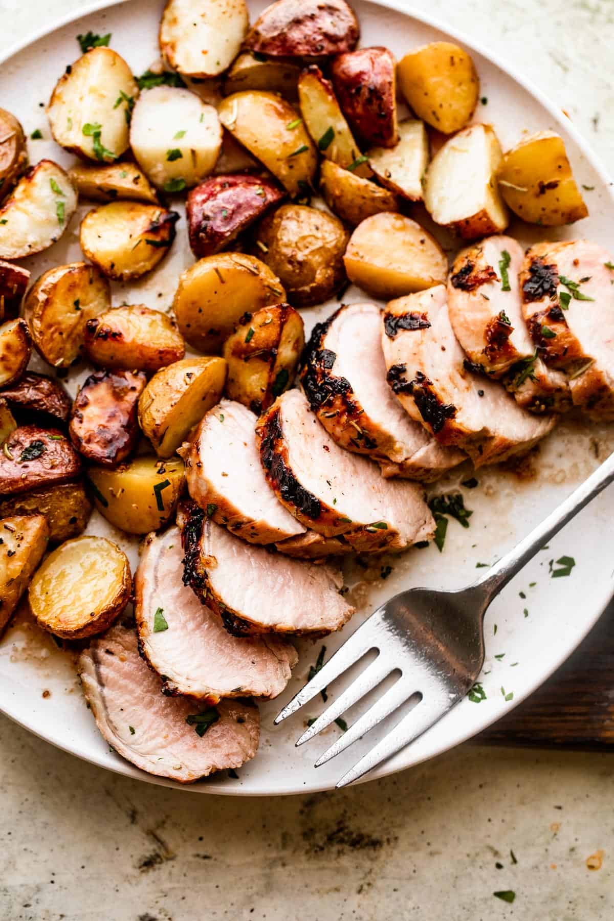 Slices of Roast Pork Tenderloin with Potatoes served on a white round dinner plate.