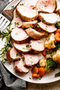 Overhead shot of Air Fryer Pork Tenderloin slices arranged on a white plate with cooked vegetables placed next to it on one side, and a large fork on the other side.