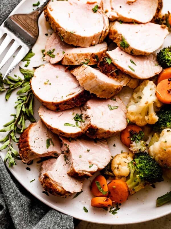 Overhead shot of Air Fryer Pork Tenderloin slices arranged on a white plate with cooked vegetables placed next to it on one side, and a large fork on the other side.