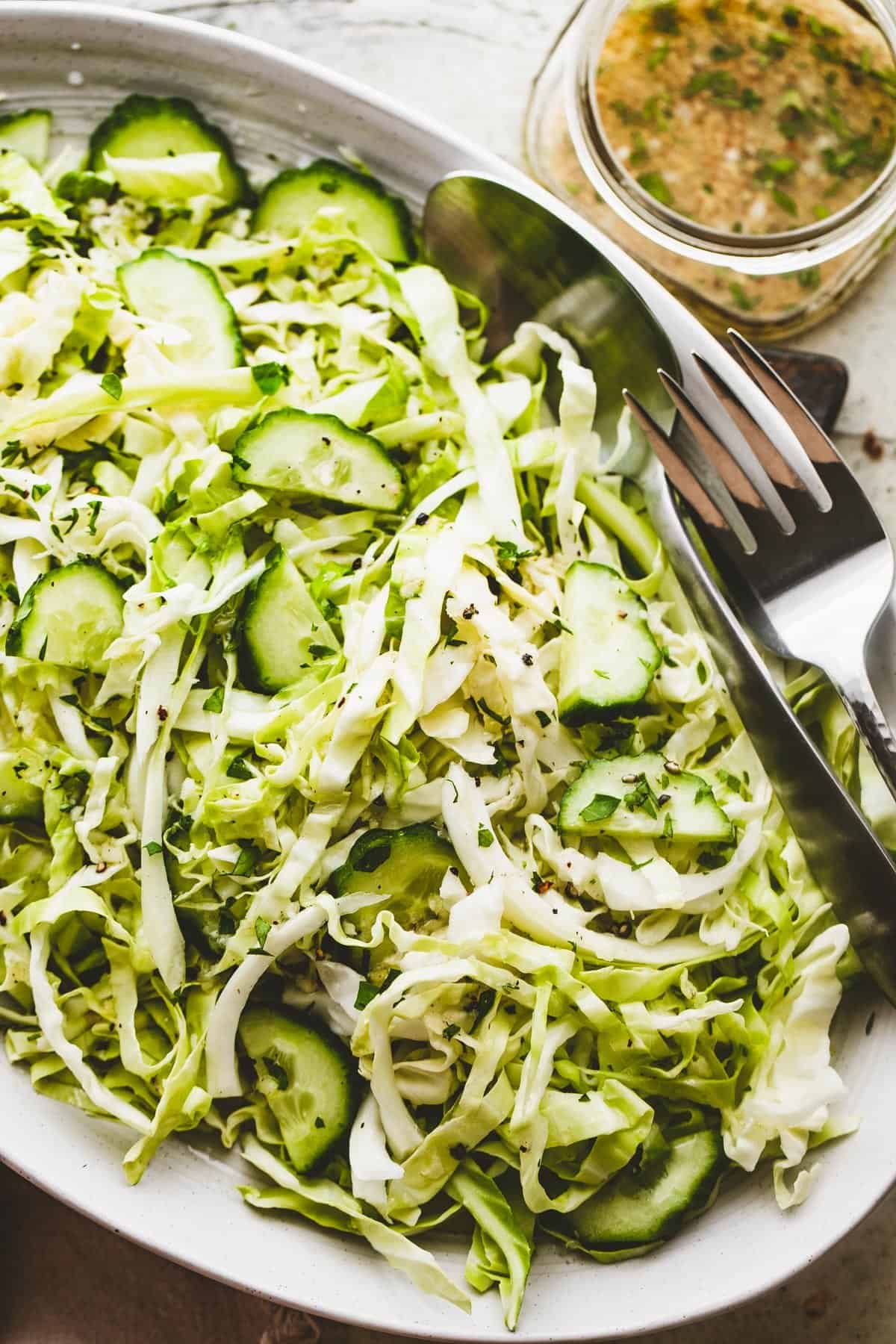 Cabbage Cucumber Salad served on an oblong serving plate with a large fork and spoon placed to the side of the salad.